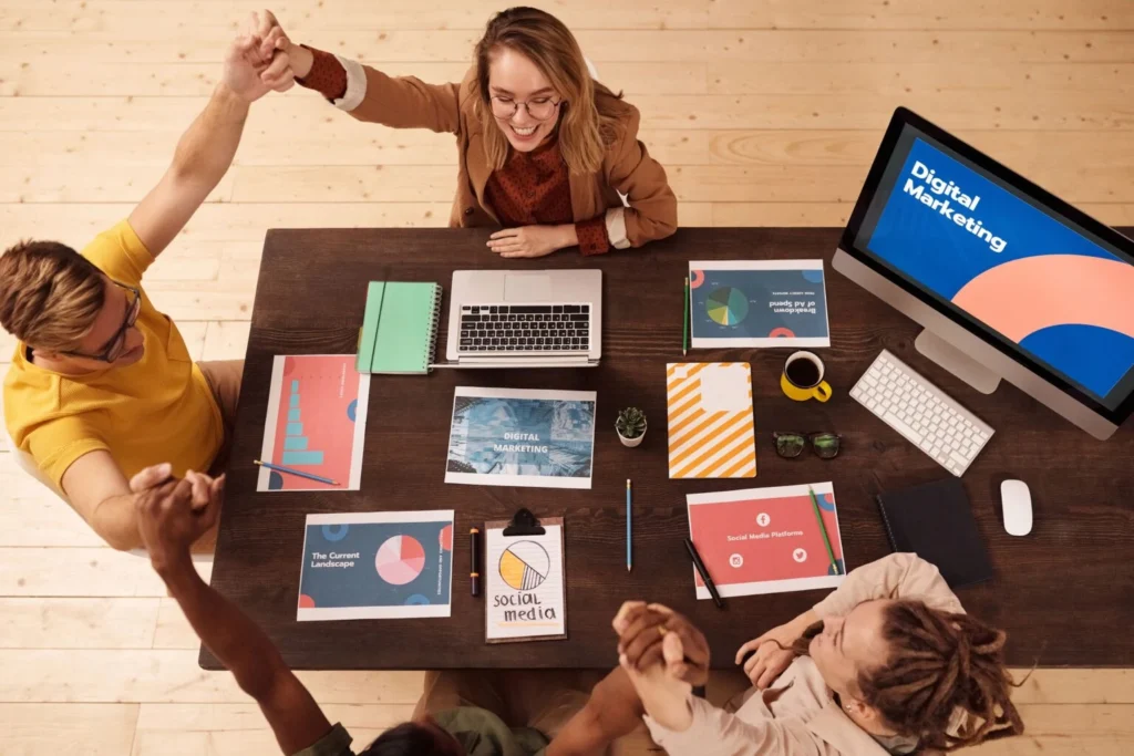 A Best Freelance Digital Marketer in Dubai ,team collaborating around a meeting table with laptops, reports, and a desktop computer in a modern office.